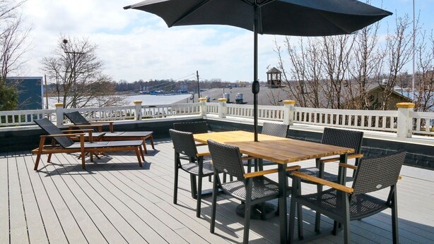 Une terrasse avec une table et des chaises, un grand parasol, et une vue sur une étendue d’eau et des bâtiments en arrière-plan.