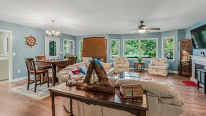 A spacious living room with a large window, a ceiling fan, and a dining area with wooden furniture. - Waterfront 4 Bed 3 Bath Sleeps 8 - Free River Cruise with Week Long Rental (Heathsville)