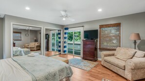 A bedroom with a bed, a sofa, a dresser, a television, and a sliding glass door leading to a balcony. - Waterfront 4 Bed 3 Bath Sleeps 8 - Free River Cruise with Week Long Rental (Heathsville)
