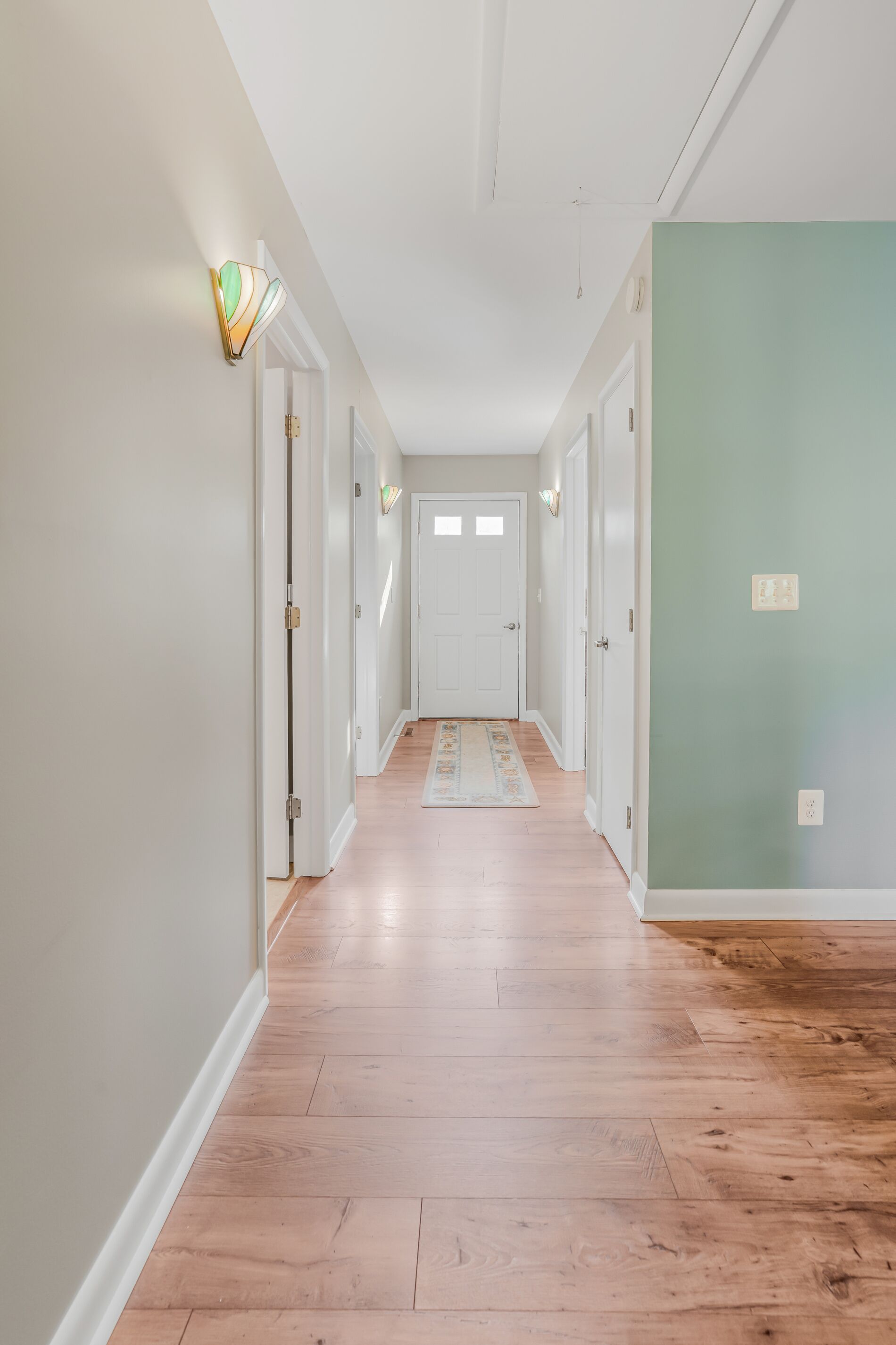 Un pasillo con piso de madera, paredes blancas y una pared verde de acento.