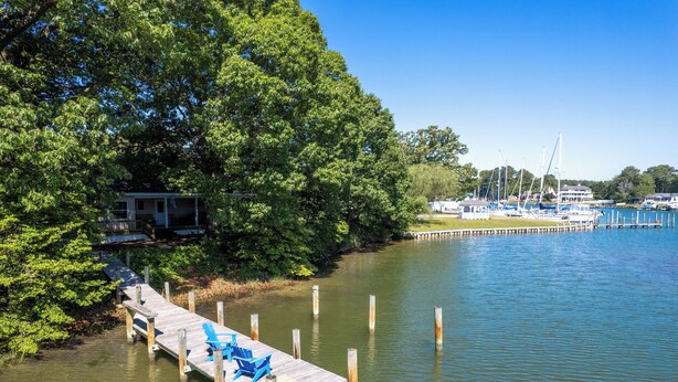 A dock with blue chairs, a small house, and boats in the background. - Waterfront 4 Bed 3 Bath Sleeps 8 - Free River Cruise with Week Long Rental (Heathsville)