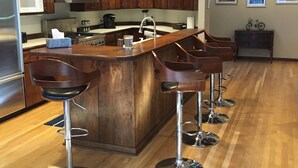 A modern kitchen with wooden cabinets, a stainless steel refrigerator, a microwave, a coffee maker, and a bar area with stools. - Fabulous Minneapolis Townhome--Large Groups (Minneapolis)