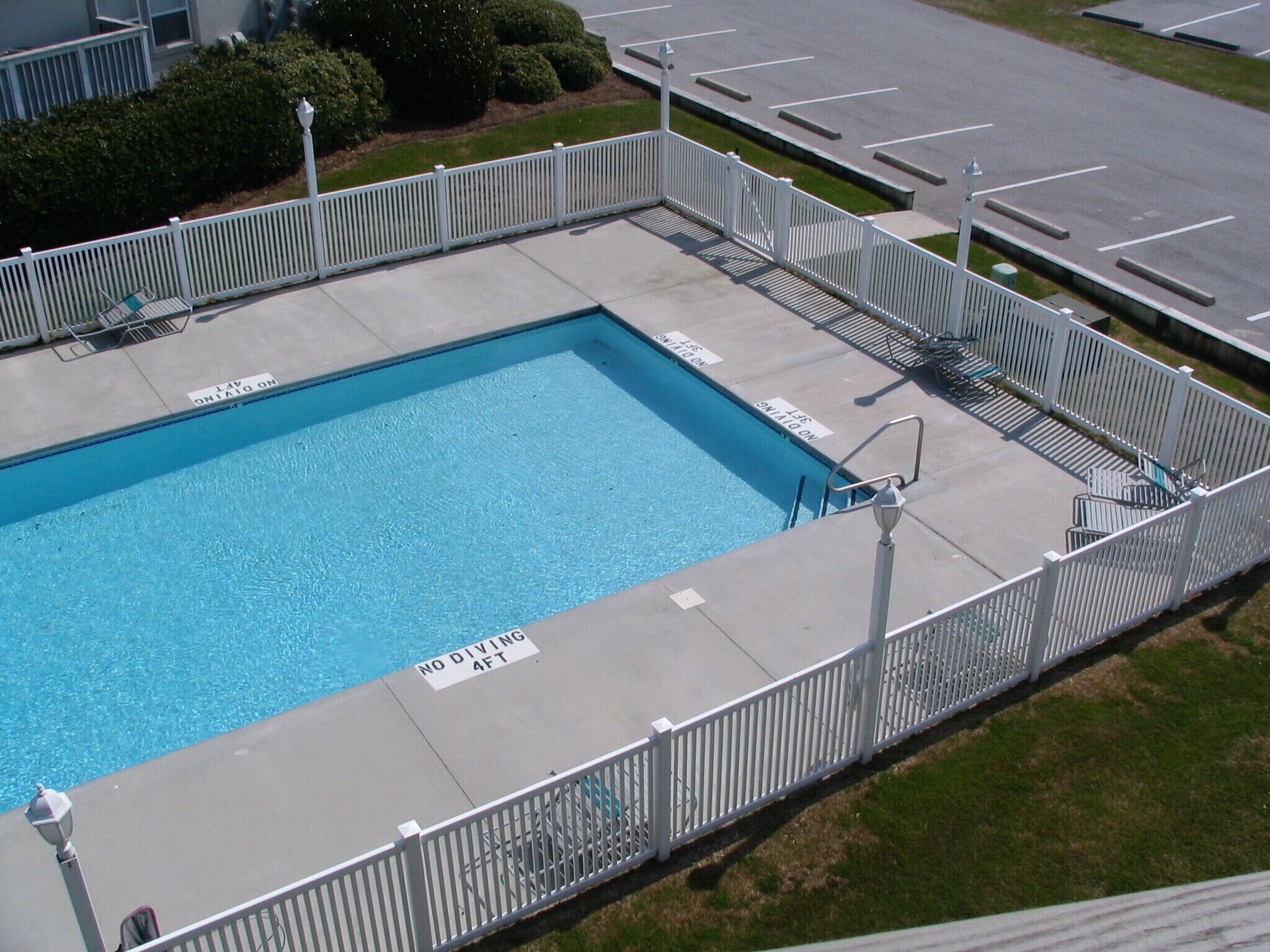 A rectangular swimming pool with a white fence, no diving signs, and a no diving 4 ft sign.