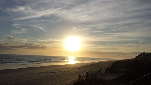 A beach with a sunset, a fence, and a building in the background.