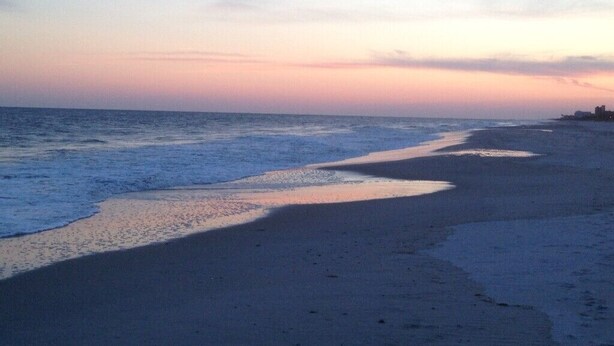 Une plage avec une mer calme et un ciel dégagé au coucher du soleil.
