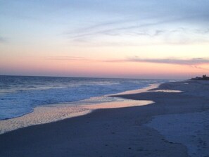 A beach with a calm sea and a clear sky at sunset.
