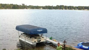 A lakeside setting with a docked boat, a campfire, and a person standing by a pole. - Papa’s Lake House, Quiet Retreat, Main Part Of Greater Bass Lake , Sleeps 12-14 (Greater Bass Lake)