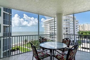 A balcony with a glass table and chairs, overlooking a beach and ocean. - Mirage: Waterfront Luxury Location  (Marco Island)