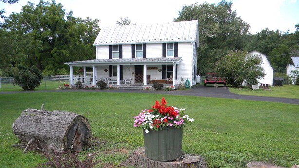 A white two-story house with a porch, surrounded by a grassy yard and trees. - Peace, quiet & relaxation!  Family friendly home. (Sugar Grove)