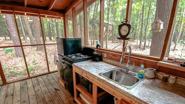 Una cabaña rústica de madera con cocina, que incluye estufa, lavamanos y un reloj en la pared.