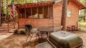 Una cabaña rústica con un porche cubierto, una parrilla y una bandera estadounidense.