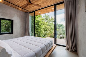 Un dormitorio con una cama grande, techo de madera y vistas a la vegetación a través de una puerta corrediza de vidrio.
