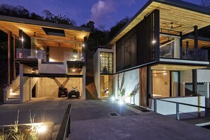 Una casa moderna de varios pisos con un amplio espacio exterior, un porche cubierto y una escalera visible que conduce a los niveles superiores.