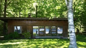 Une cabane moderne en bois, dotée de grandes fenêtres et entourée d’une végétation luxuriante.