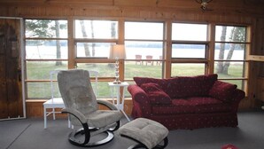Une pièce avec un plafond en bois, un canapé rouge, un fauteuil gris et une petite table avec une lampe.