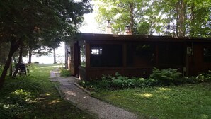 Un chalet rustique en bois, accessible par un chemin de gravier, entouré d’une végétation luxuriante et d’arbres.