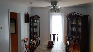 A dining room with a wooden table, chairs, a ceiling fan, a cabinet, and a door leading to another room. - Ocean Front House in Newfoundland (Cook's Harbour)