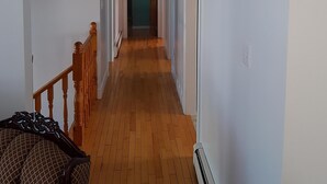 A narrow hallway with wooden flooring, white walls, and a green door at the end. - Ocean Front House in Newfoundland (Cook's Harbour)