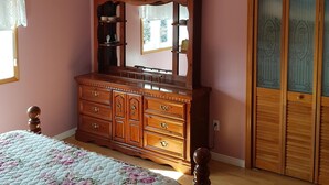 A bedroom with a wooden dresser, a ceiling fan, a bed with a floral quilt, and a wooden wardrobe with glass doors. - Ocean Front House in Newfoundland (Cook's Harbour)