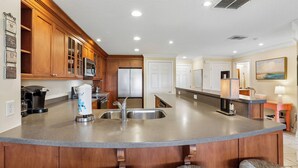 Una cocina con gabinetes de madera, un refrigerador de acero inoxidable, una isla integrada con un lavamanos y una cafetera.