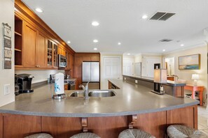 A kitchen with wooden cabinets, a stainless steel refrigerator, a built-in island with a sink, and a coffee maker.