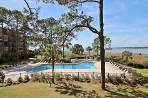 A swimming pool with lounge chairs, surrounded by trees and a view of the water.