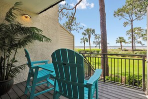 Un balcon agrémenté de deux fauteuils Adirondack turquoise, d’un pot de fleurs et offrant une vue sur une pelouse et des arbres bien entretenus.