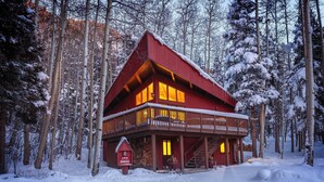 En röd stuga med en balkong, omgiven av snötäckta träd.