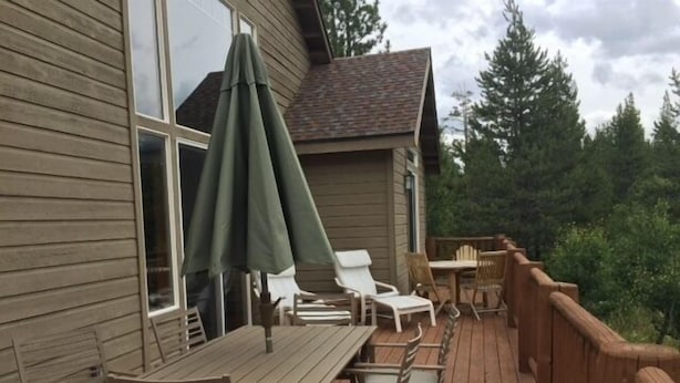 A wooden deck with a table and chairs, an umbrella, and a view of trees.