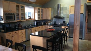 A kitchen with wooden cabinets, a central island, black chairs, and a stainless steel refrigerator.