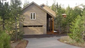 A single-story wooden house with a garage, surrounded by trees.