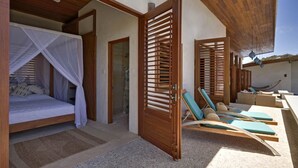 Ein Zimmer mit einem Bett, einem Moskitonetz, Holztüren und einer Sitzecke mit Lounge-Stühlen.