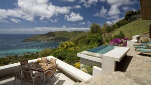 Eine Terrasse mit Esstisch und Stühlen, ein kleiner Pool und Meer- und Hügellandschaft.