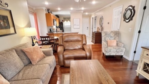 Una sala de estar con un sofá, un sillón de cuero marrón, un sillón estampado y una mesa de centro de madera.