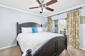 Relax in a serene bedroom with a comfortable bed, ceiling fan, and a large window offering a view of lush greenery.