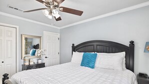 Un dormitorio con cama, mesita de noche, cómoda, ventilador de techo y espejo.