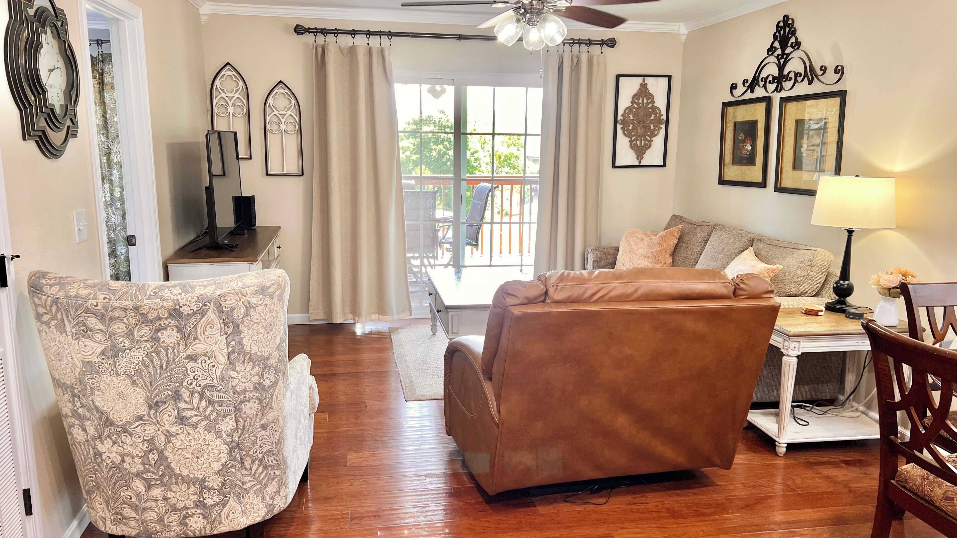 A living room with a brown leather sofa, patterned armchair, and a white side table with a lamp.