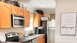 Una cocina con armarios de madera, encimera de granito, dos taburetes de bar, un refrigerador y un letrero en la pared.