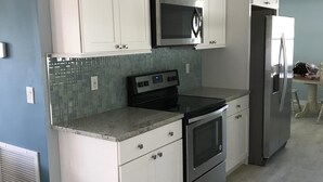 A modern kitchen with white cabinetry, a stainless steel microwave, a built-in oven, and a refrigerator. - Newly Renovated Coastal Style house (Sebastian)