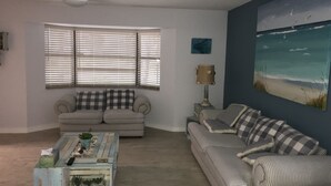 A living room with a striped sofa, a checkered sofa, a wooden coffee table, and a painting of a beach scene. - Newly Renovated Coastal Style house (Sebastian)