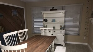 A dining area with a wooden table and white chairs, a white bench, and a white cabinet with shelves. - Newly Renovated Coastal Style house (Sebastian)