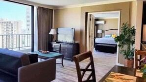Habitación de hotel con un ventanal grande, una cama, un escritorio con lámpara, una silla y una mesa de comedor.