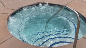 Una piscina amb una banyera d'hidromassatge al centre, envoltada de gandules i una tanca.