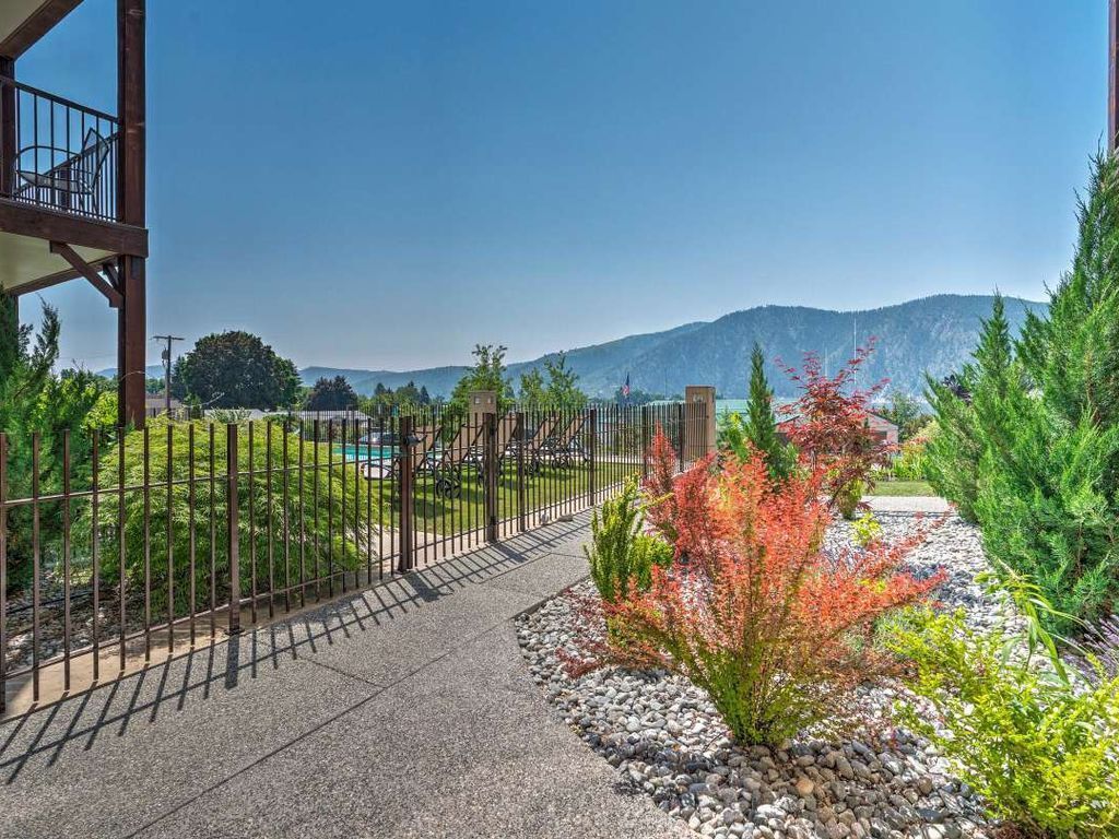 A pathway leading to a building with a metal fence, surrounded by greenery and a mountain in the background.