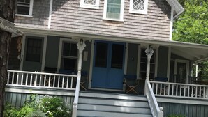 A two-story house with a front porch, a blue door, and a gravel driveway. - Family & dog friendly; walk to beach, cliff, town, ferries, all bedrooms w/AC (Oak Bluffs)