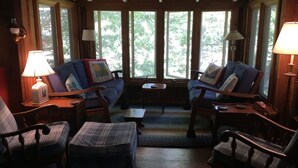 A cozy room with a sofa, chairs, and a small table. Large windows allow natural light and views of trees. - Family & dog friendly; walk to beach, cliff, town, ferries, all bedrooms w/AC (Oak Bluffs)