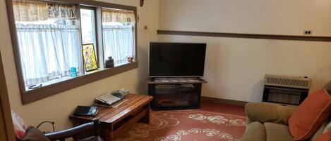 A living room with a sofa, a wooden chair, a small table, a television, and a decorative rug.