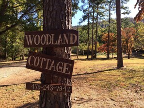 Un letrero de madera con la inscripción 'WOODLAND COTTAGE' y un número de teléfono.
