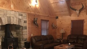 A cozy log cabin interior with a stone fireplace, leather sofas, and a wooden dining table. - Ticket to the great outdoors! (Heavener)