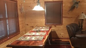 A wooden interior with a dining table, benches, a hanging light fixture, and a wall-mounted lamp. - Ticket to the great outdoors! (Heavener)